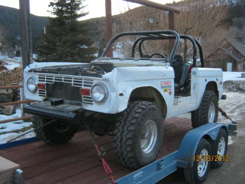 1970 Ford Bronco - A white 1970 Ford Bronco with a roll cage is loaded onto a trailer in a snowy, rural setting.
