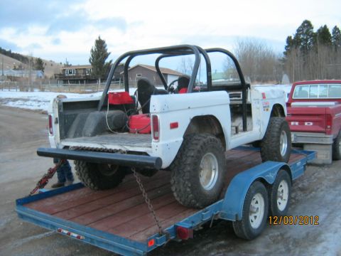 1970 Ford Bronco - A white 1970 Ford Bronco is loaded onto a trailer, showing its roll cage and two red gas cans in the bed.