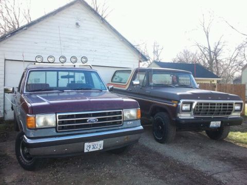 1979 Ford Bronco - Two Ford trucks are parked side-by-side in front of a white garage, with the 1979 Ford Bronco on the right.