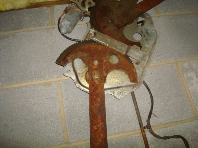 Rusty window regulator mechanism with motor and gears against a cinder block wall