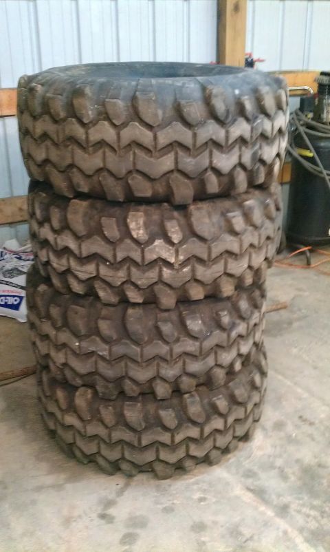 1995 Ford Bronco - Four off-road tires are stacked in a garage or workshop setting.