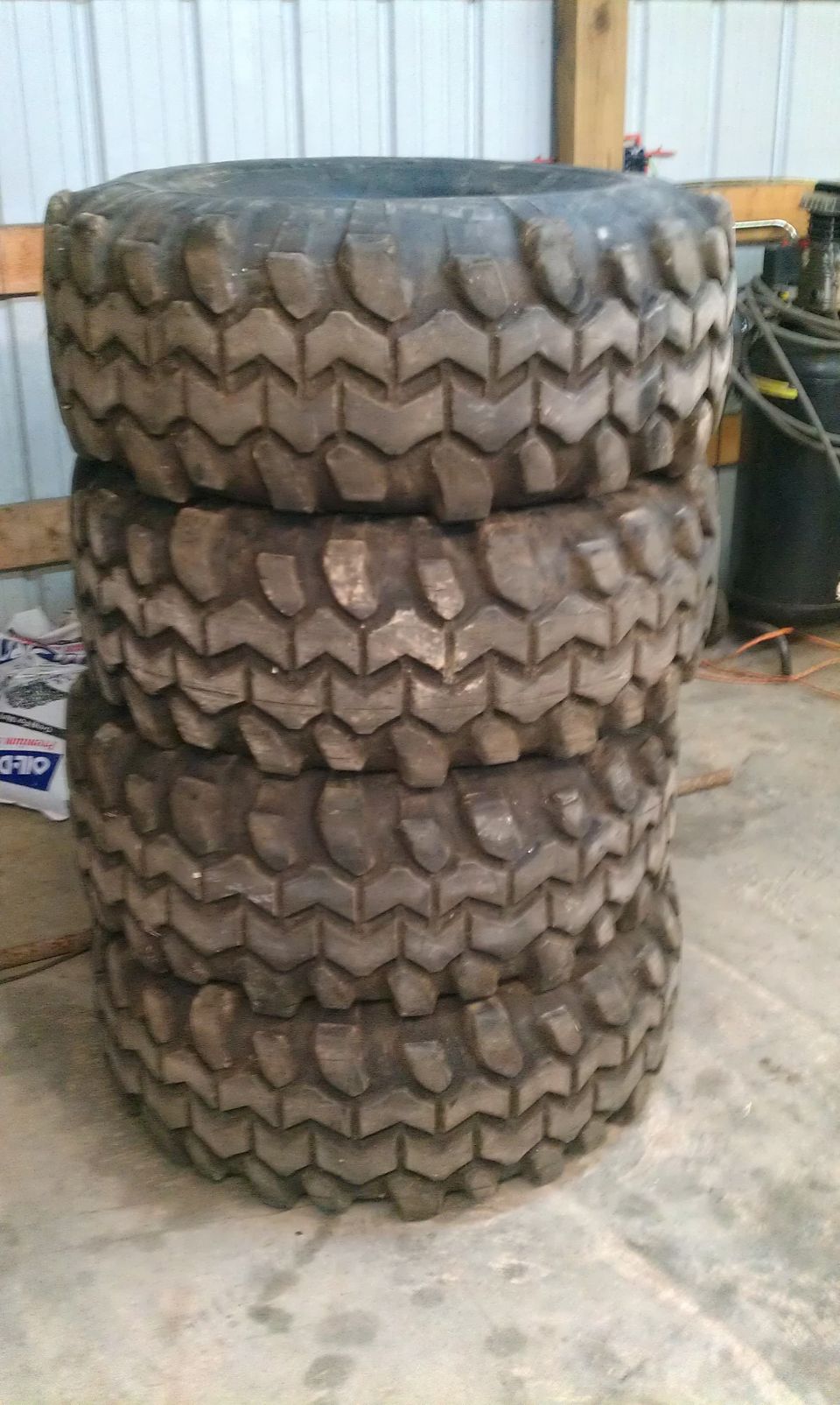 Stack of four large off-road tires with aggressive tread pattern