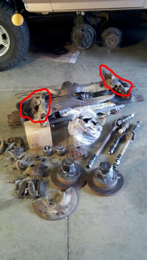 1995 Ford Bronco - Disassembled vehicle parts are laid out on a concrete floor, with a portion of a vehicle's undercarriage visible above.