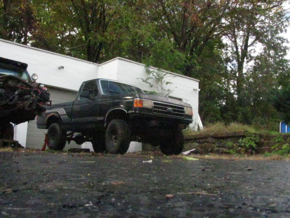 Black pickup truck on jacks, another vehicle's engine in foreground