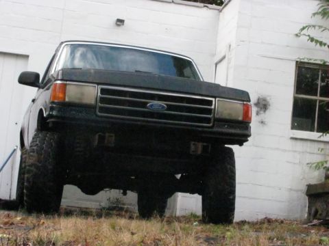 1994 Ford F-150 - A dark Ford F-150 pickup truck is parked in front of a white building with a window.