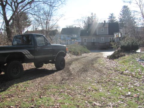 1994 Ford F-150 - A lifted pickup truck sits on a gravel driveway with houses in the background.