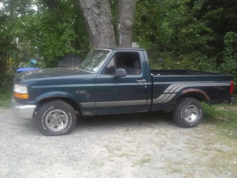1994 Ford F-150 - Side view of a dark green Ford F-150 pickup truck parked outdoors with trees in the background.