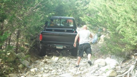 1994 Ford F-150 - A black pickup truck navigates a rough, rocky path surrounded by trees.