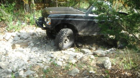 1994 Ford F-150 - A black off-road vehicle with large tires is seen navigating a rocky, wooded area.
