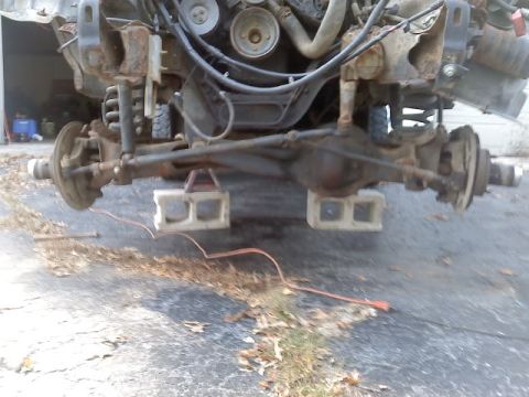 1994 Ford F-150 - Front axle and engine components of a truck are visible, with the vehicle supported by cinder blocks.