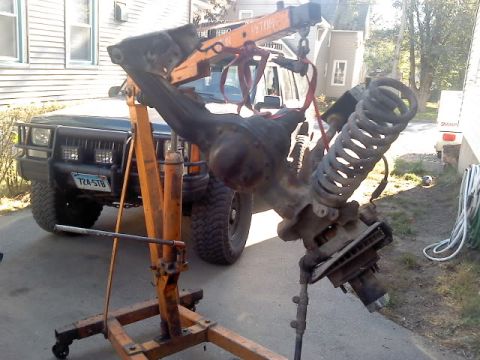 1994 Ford F-150 - A front axle assembly is hoisted above a Jeep Cherokee, suggesting a modification or repair.