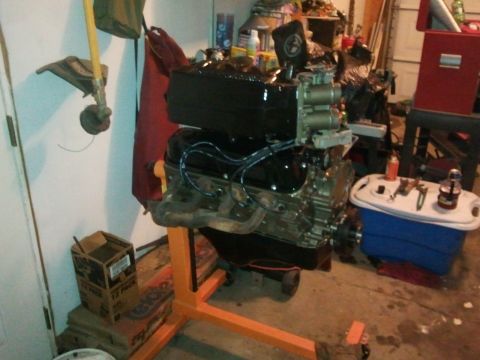1990 Ford Bronco - Engine on an orange stand in a garage, with tools and supplies nearby.