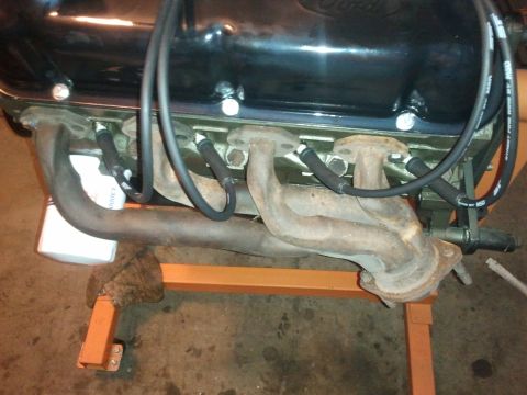 1990 Ford Bronco - Close-up view of an engine's exhaust manifold and spark plug wires, mounted on an orange stand.