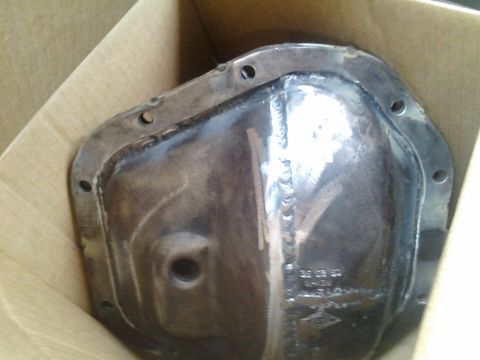 1968 Ford Bronco - Differential cover with visible welds and some stamped numbers, sitting in a box.