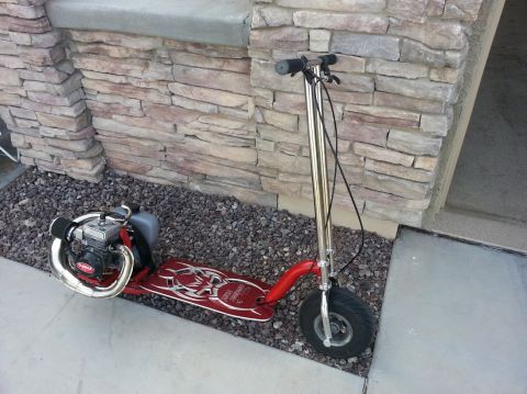 1978 Ford Bronco - A red motorized scooter with a gas engine is parked outside a building.
