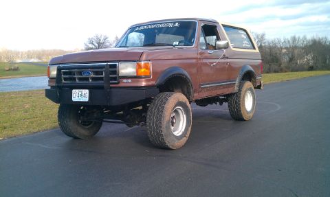 1987 Ford Bronco - This 1987 Ford Bronco features a prominent front push bar and 4x4 badging, seen from a three-quarter front angle.