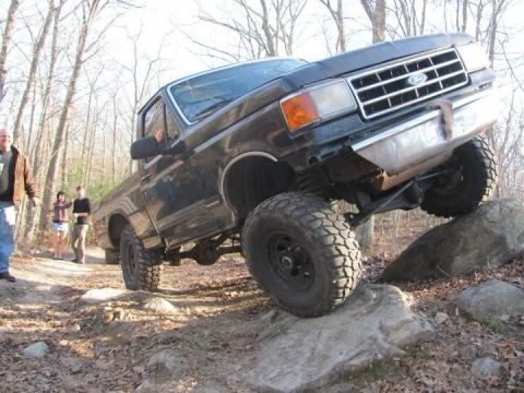 1994 Ford F-150 - A lifted Ford truck navigates a rocky off-road course with onlookers present.