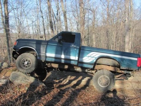 1994 Ford F-150 - Teal Ford F-150 pickup truck with off-road tires navigating rocky terrain.