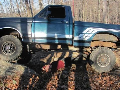 1994 Ford F-150 - A person is on the ground under a blue pickup truck that is on a rocky, wooded trail.