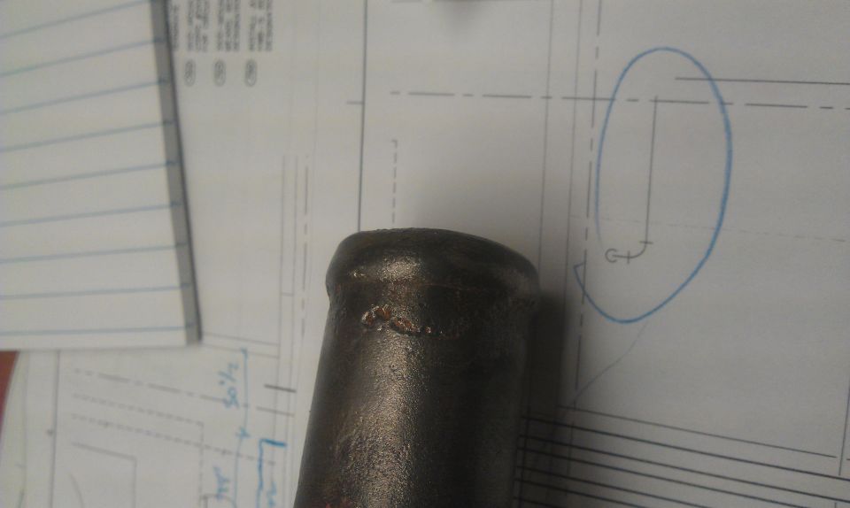 Metal pipe resting on blueprints with handwritten notes and a circled diagram