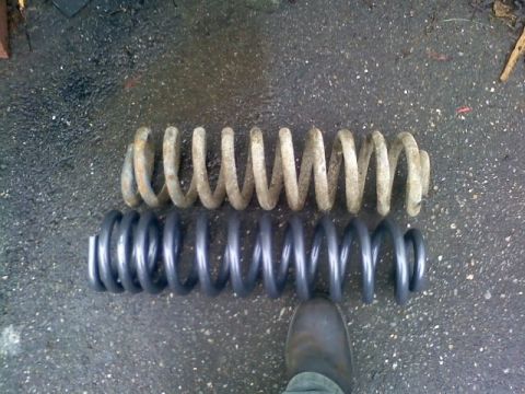 1994 Ford F-150 - Comparison of a rusty old coil spring with a new, dark gray coil spring, with a boot visible at the bottom.