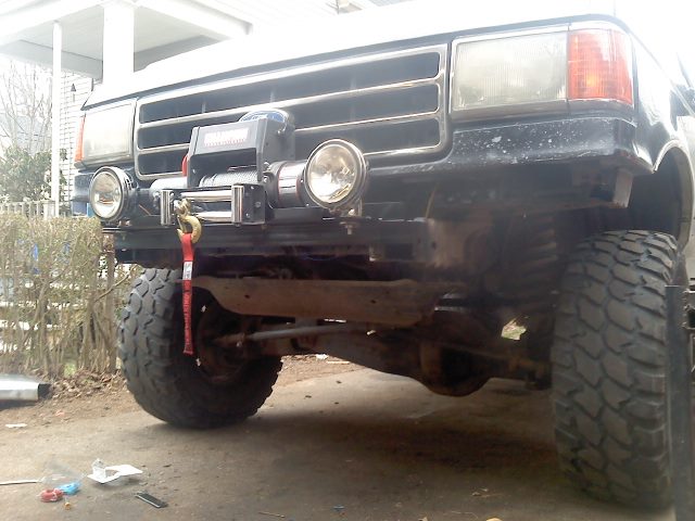 Truck front end with large tires, winch, and auxiliary lights. The grille and headlight design suggest a 1992-1996 Ford F-Series