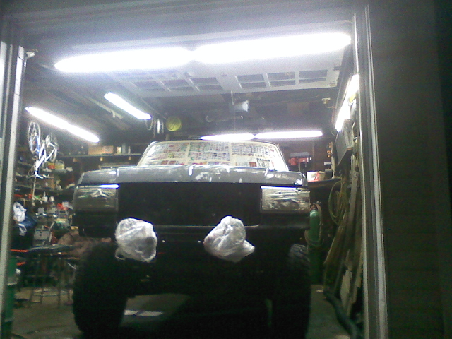 Front view of a dark-colored truck parked inside a garage, with its windshield covered in paper