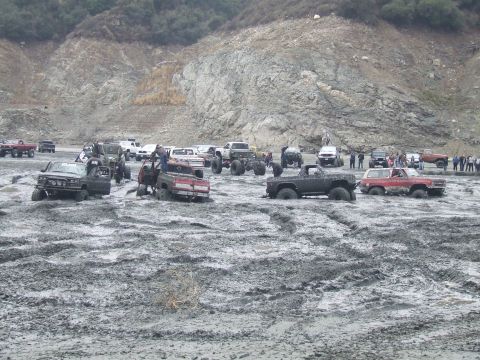 1978 Ford Bronco - Several off-road vehicles are bogged down in a muddy terrain with spectators observing the scene.