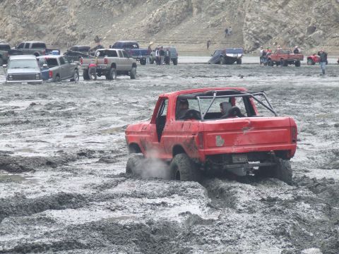 1978 Ford Bronco - A red 1978 Ford Bronco is stuck in thick mud, with other vehicles visible in the background at a muddy off-road event.