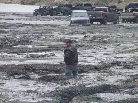 1978 Ford Bronco - Multiple vehicles are stuck in a muddy area, with a man standing in the foreground.