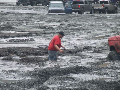 1978 Ford Bronco - Multiple vehicles are stuck in deep mud as a man wades through the mire.