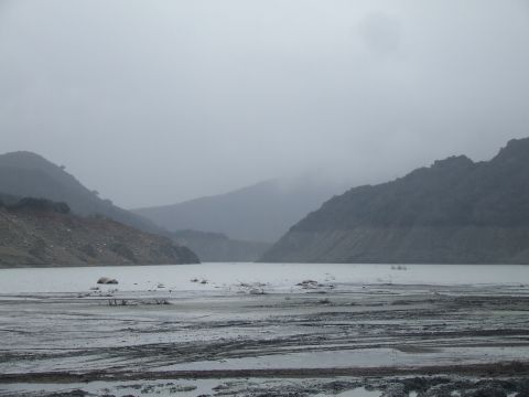 1978 Ford Bronco - A hazy view of a lake surrounded by hills, with a muddy, tire-tracked foreground.