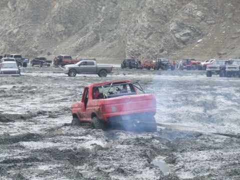 1978 Ford Bronco - Multiple off-road vehicles are gathered in a muddy area, with one red Ford Bronco deeply stuck.