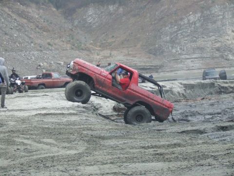 1978 Ford Bronco - A red 1978 Ford Bronco navigates a muddy terrain, with other vehicles visible in the background.