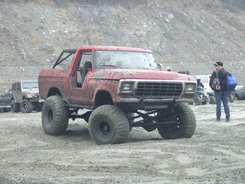 1978 Ford Bronco - Modified 1978 Ford Bronco covered in mud, parked outdoors with other vehicles and a person in the background.