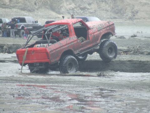 1978 Ford Bronco - Mud-covered 1978 Ford Bronco navigates a muddy terrain with other vehicles in the background.