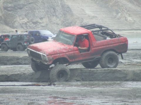 1978 Ford Bronco - A red 1978 Ford Bronco navigates a muddy obstacle course with other vehicles in the background.