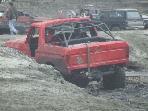 1978 Ford Bronco - A red 1978 Ford Bronco is partially submerged in mud, its rear end visible with a roll cage installed.