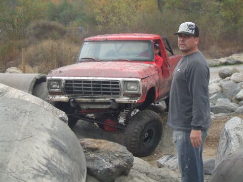 1978 Ford Bronco - A man stands next to a red 1978 Ford Bronco as it maneuvers over a rocky terrain.