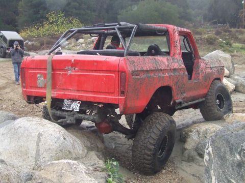 1978 Ford Bronco - Mud-covered 1978 Ford Bronco navigating rocks with a roll cage installed. Another vehicle is in the background.