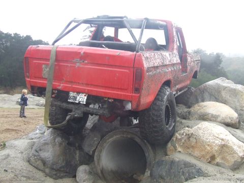 1978 Ford Bronco - A red 1978 Ford Bronco navigates a rocky obstacle course, its body covered in mud.