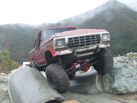 1978 Ford Bronco - A muddy 1978 Ford Bronco navigates a challenging off-road course with steep, fog-covered hills in the background.