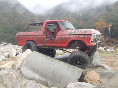 1978 Ford Bronco - This heavily modified 1978 Ford Bronco is shown tackling a challenging off-road course with large rocks and obstacles.