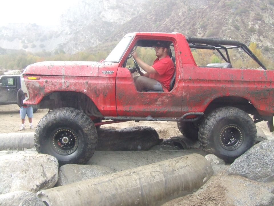Red 1978 Ford Bronco with large tires navigating rocky terrain