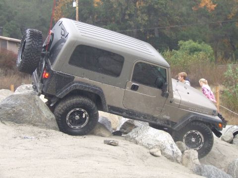 1978 Ford Bronco - A Jeep Wrangler Rubicon navigates a rocky obstacle course with two children observing from the hood.