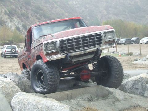 1978 Ford Bronco - This red 1978 Ford Bronco is shown off-roading over rocks, with another white SUV visible in the background.