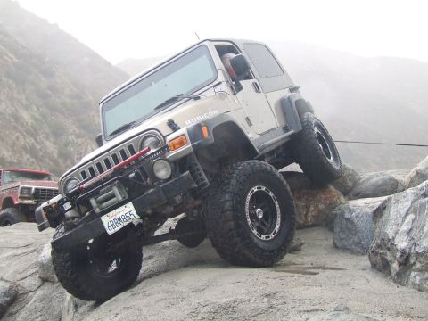 1978 Ford Bronco - A Jeep Wrangler Rubicon navigates a rocky trail, with a red truck visible in the background.