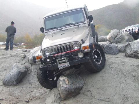 1978 Ford Bronco - A Jeep Wrangler TJ is shown off-roading over large rocks, with another Jeep in the distance.