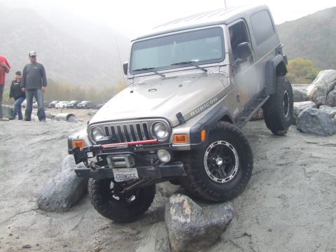 1978 Ford Bronco - A Jeep Wrangler Rubicon navigates a rocky terrain with several people observing and other vehicles in the distance.