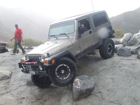 1978 Ford Bronco - A tan Jeep Wrangler Rubicon is shown off-roading on a rocky, uneven surface.